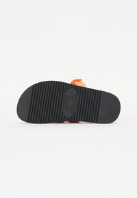 Svart gummisula med upphöjda spår och en cirkulär logotyp. Orange detaljer syns på hälen. Den övergripande designen är enkel och funktionell.
