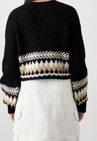 Czarny dziergany sweter o krótkim kroju, z poziomym wzorem białych i beżowych diamentów na dole oraz na rękawach.
