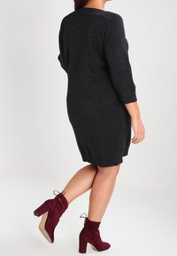 Robe pull en tricot gris charbon à manches trois-quarts, associée à des bottines bordeaux à talon épais avec des détails en dentelle.