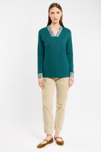 Haut teal à manches longues avec un décolleté en V et un col à motif, associé à un pantalon beige et des ballerines marron. La tenue présente des détails de poignets contrastants.