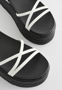Zwarte platformsandalen met witte kruiselingsbandjes, gekenmerkt door een gladde textuur en ronde hoeken, ontworpen voor een eigentijdse uitstraling.