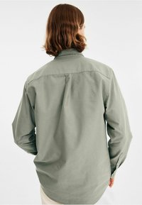Groene longsleeve shirt van een gladde stof, met een achterpand naad, knopenmanchetten en een relaxte pasvorm.