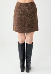 Bruine textuur mini-rok met een getailleerd silhouet. Gecombineerd met hoge zwarte leren laarzen met hak, met een gladde afwerking en een gestroomlijnd ontwerp.