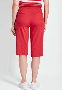 Rote Bermudashorts aus leichtem Material mit geradem Schnitt, Gesäßtaschen und einem Saum just über dem Knie. Kombiniert mit weißen Sneakern.