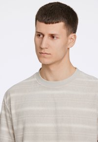 Camisa de color gris claro, texturizada, con rayas horizontales y un escote redondeado. Tela suave con un patrón sutil. Diseño casual.