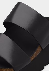 Μαύρο σανδάλι με δύο φαρδιές δερμάτινες λουρίδες και πάτο από φελλό σε μαύρη σόλα.