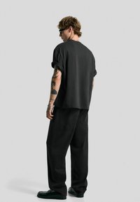 Schwarzes, übergroßes T-Shirt mit umgeschlagenen Ärmeln, kombiniert mit lockeren schwarzen Hosen. Das Outfit weist subtile Texturdetails und ein minimalistisches Design auf.