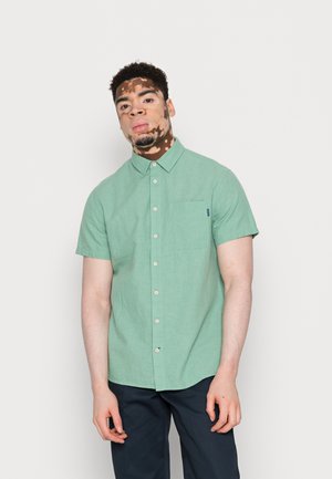 Camicia a maniche corte, di colore verde chiaro, con bottone e taschino, realizzata in tessuto di lino. Caratterizzata da colletto classico e piccolo logo decorativo.