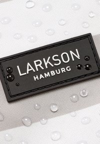 Fekete téglalap alakú címke "LARKSON HAMBURG" felirattal, fehér textúrált szöveten vízcseppekkel.