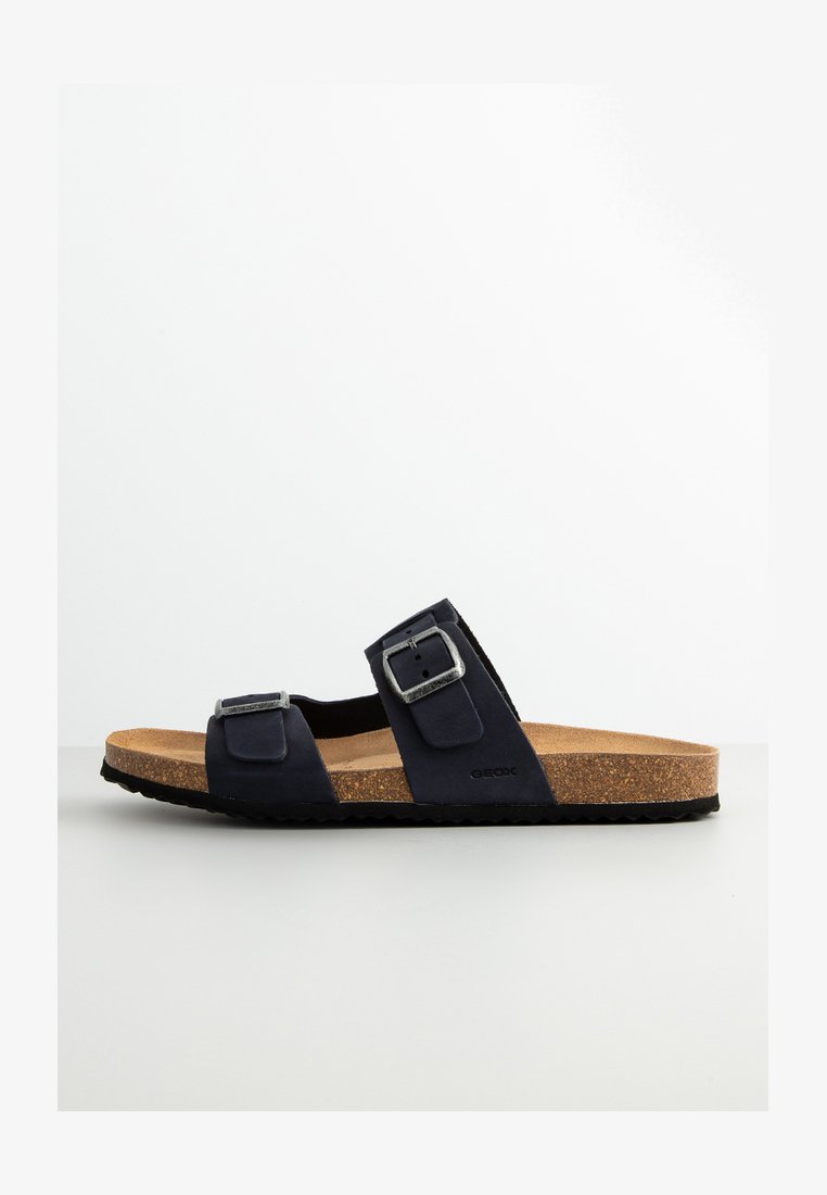 Sandali a scivolo in suede blu navy con due fibbie regolabili, intersuola in sughero e suola esterna in gomma nera strutturata. Logo Geox sul lato.