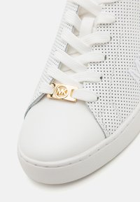 Hvide sneakers med perforeret overdel, flade hvide snørebånd og et guld logo-accent. Rundet tå med en holdbar gummisål.