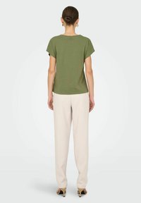 T-shirt à manches courtes vert olive avec une coupe décontractée, associé à un pantalon large crème et des talons noirs, vu de dos.