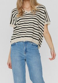 Randig stickad topp i beige med svarta ränder, med v-ringning och korta ärmar. Kombinerad med ljusblå högmidjade jeans.