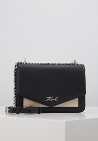 Borsa a tracolla in pelle nera con accenti beige, tracolla a catena, logo impresso sul davanti e forma a busta strutturata.