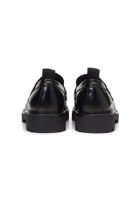 Zwarte leren schoenen met een dikke zwarte rubberen zool, met elastische accenten bij de hiel voor gemakkelijkere instap. Glad oppervlak met minimale details.