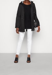 Černá bunda s kapucí a kostkovanou podšívkou, doplněná o černý top, bílé džíny a černé boty s otevřenou špičkou. Jednoduchý design.