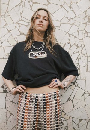 Czarny oversizeowy t-shirt z haftowanym wzorem, zestawiony z wielokolorowymi, wzorzystymi spodniami z motywem fal. Obecne srebrne dodatki biżuteryjne.