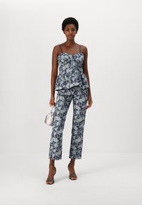 Tumedat floral peplum-top heles sinise ja heleda sinise lilledega, mis on kombineeritud sobivate lillemusterdate pükste ja õhukeste rihmadega. Lisatud on läikiv hõbedane kott.
