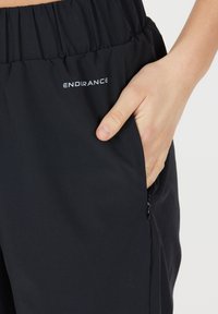 Svarta sportshorts med elastisk midja, med en sidoficka med dragkedja och vit "ENDURANCE" logotyp på framsidan.