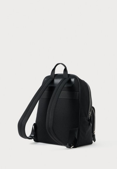 Black backpack with mesh texture, padded shoulder straps, and a top handle. Features a zippered closure and side pocket for storage.