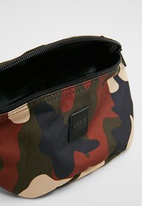 Borsetta mimetica realizzata in tessuto resistente; presenta una chiusura con zip, una fodera interna e un piccolo logo in rilievo sulla parte anteriore.