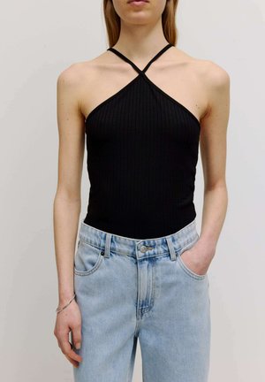 Zwarte ribbel haltertop met gekruiste bandjes, gecombineerd met hooggerende lichtblauwe denim jeans met een knoopsluiting en zijzakken.