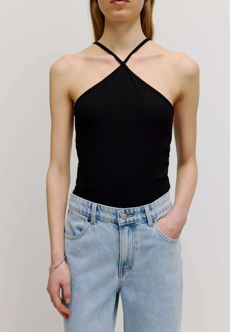 Zwarte ribbel haltertop met gekruiste bandjes, gecombineerd met hooggerende lichtblauwe denim jeans met een knoopsluiting en zijzakken.