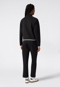 Czarny dres sportowy z wysokim kołnierzem, prążkowanymi mankietami i białym akcentem w talii. Noszony z białymi trampkami z czarnym logo.