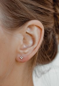 Orecchino a bottone in oro rosa con un design floreale, caratterizzato da quattro piccole pietre preziose trasparenti disposte in un motivo geometrico. Finitura metallica testurizzata.