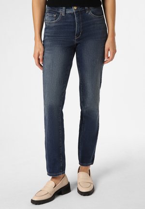 Dunkelblaue Denim-Jeans mit geradem Schnitt, versehen mit Fronttaschen und einer subtilen, leicht ausgewaschenen Textur. Kombiniert mit hellbeigen Slippern.