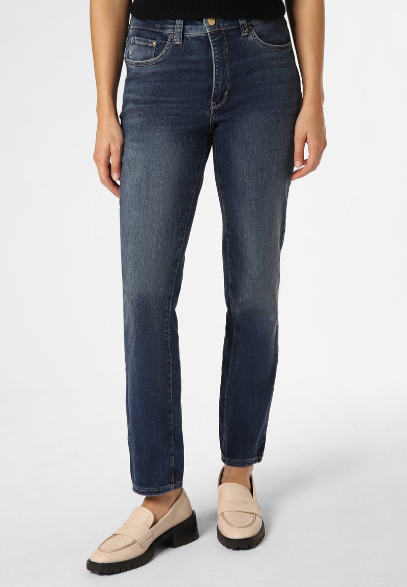 Jeans en denim bleu foncé avec une coupe droite, comportant des poches avant et une texture légèrement délavée. Associés à des mocassins beige clair.