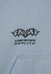 Jasnoniebieska bluza z kapturem, zdobiona czarnym graficznym wzorem z ostrymi, splątanymi kształtami oraz napisem "UNKNOWN REALITY" poniżej. Miękka struktura materiału.