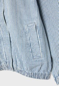 Zbliżenie na niebiesko-białą kurtkę z pionowymi paskami, z boczną kieszenią na rozporek i elastycznym zakończeniem u dołu.