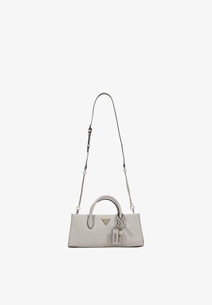 Bolso rectangular pequeño de color beige con asas superiores, correa delgada para el hombro desmontable con detalles de cadena y una etiqueta de la marca Guess adjunta.
