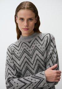 Grau gestrickter Pullover mit einem Zickzackmuster in Schwarz und Grau. Verfügt über einen gerippten Rundhalsausschnitt und lockere Ärmel. Weiche Textur.