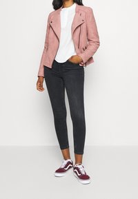 Ljusrosa mockajacka i motorcykelstil med silverdetaljer, bärs över en vit topp och svarta smala jeans, tillsammans med vinröda sneakers.