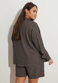 Tummanharmaa kuvioitu lyhythihainen paita rennolla istuvuudella, yhdistettynä samankaltaisiin shortseihin. Napit yksityiskohtana paidan hihassa.