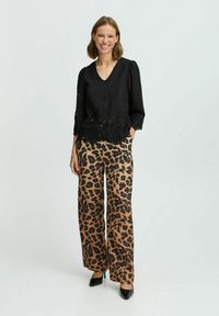 Blouse noire brodée avec un décolleté en V et des manches trois-quarts, associée à un pantalon large imprimé léopard en beige et noir, complété par des talons hauts.
