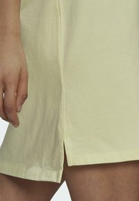 Light yellow cotton dress with a side slit. Soft texture and relaxed fit enhance comfort. Visible stitching along the hem and slit.