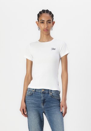 T-shirt en coton blanc à côtes avec des manches courtes, un col rond et un petit logo sur la poitrine gauche. Associé à un jean en denim bleu.