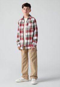 Rood, groen en witte geruite flanellen shirt, beige cargobroek en witte sneakers. Heeft een borstzak en een casual pasvorm.