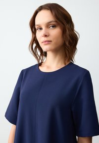Abito blu navy a maniche corte con scollatura rotonda e dettagli di cucitura sottili. Tessuto liscio con una vestibilità comoda, senza motivi o accenti visibili.