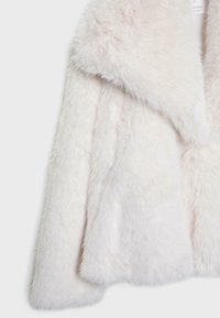 Manteau en fausse fourrure blanche douce avec col large et manches longues, gros plan montrant la texture et le matériau pelucheux.