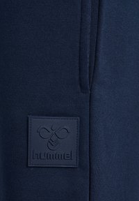 Navyblauwe sportshorts van een textuurovergetrokken stof met een rechthoekig geborduurd logo-embleem met een bijontwerp en de merknaam "hummel."