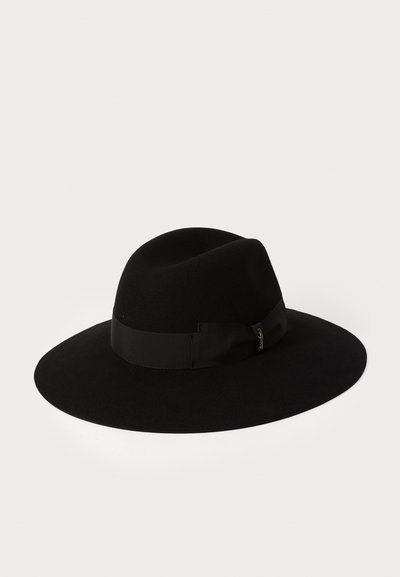 Chapeau en feutre noir avec un large bord et un bandeau en ruban présentant un détail en nœud. Le chapeau a une texture lisse et une forme structurée.