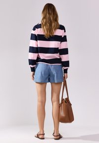 Maglione a maniche lunghe a righe navy e rosa abbinato a pantaloni shorts di jeans chiari. Borsa marrone con doppi manici e texture liscia.