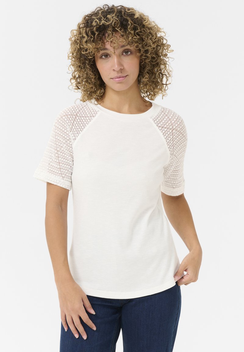 T-shirt blanc à manches courtes présentant un tissu texturé et en maille sur les manches et un col rond. Coupe légèrement décontractée, assorti avec un jean sombre.