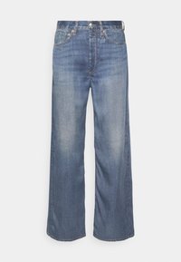 Jean en denim bleu à jambes larges avec un lavage délavé, comportant cinq poches, une fermeture à bouton et des détails de couture contrastants.