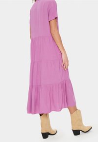 Rosa midiklänning med korta ärmar, lagerdesign och volangkant. Bärs med beige cowboystövlar. Slätt tyg med en subtil lyster.