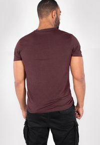 Bordeauxrotes, enges T-Shirt aus weichem Stoff mit kurzen Ärmeln und einem Rundhalsausschnitt, getragen mit schwarzen Cargohosen. Glatte Textur, minimale Detailgestaltung.
